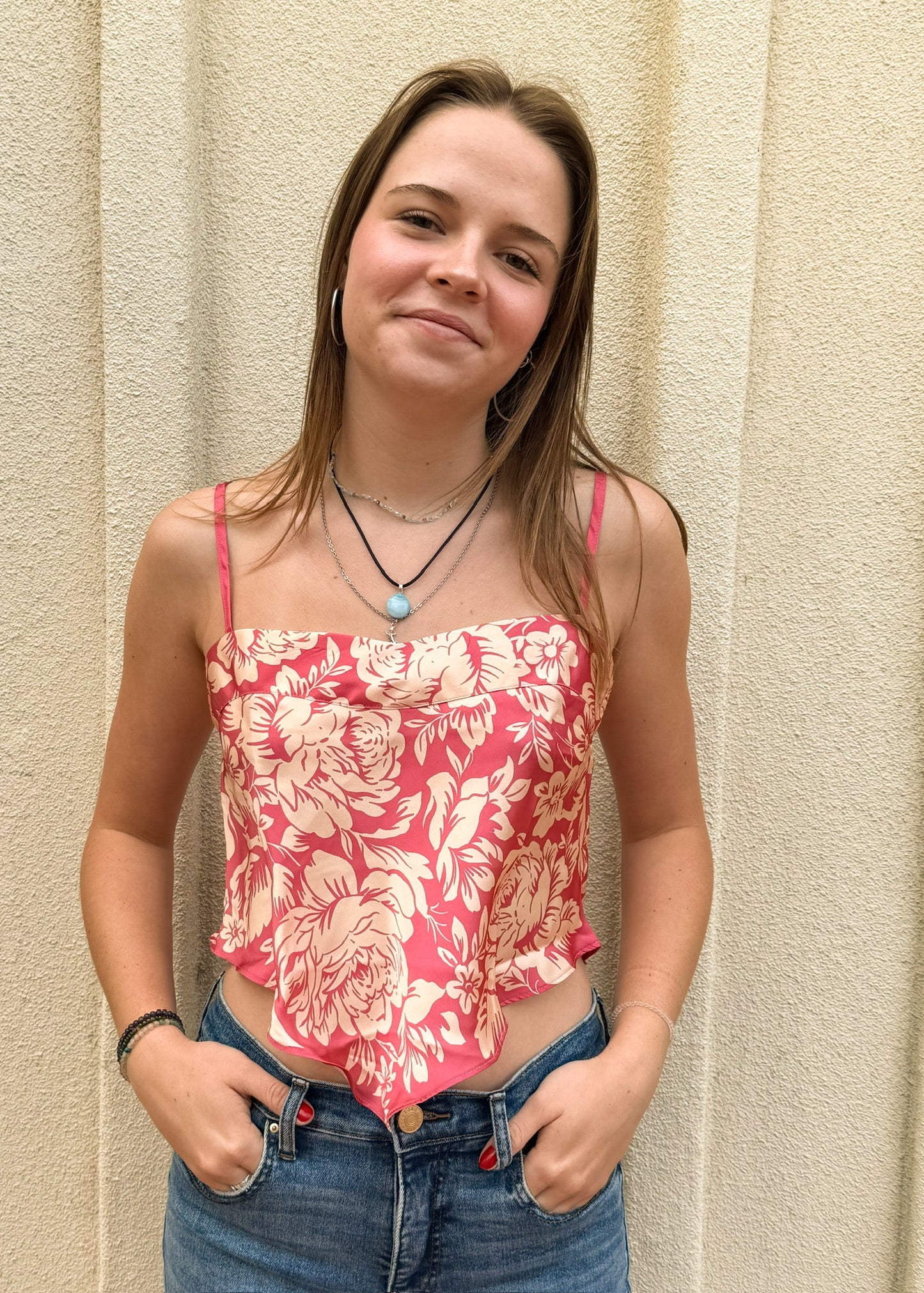 Young woman wearing a floral pink top and blue jeans against a beige wall.