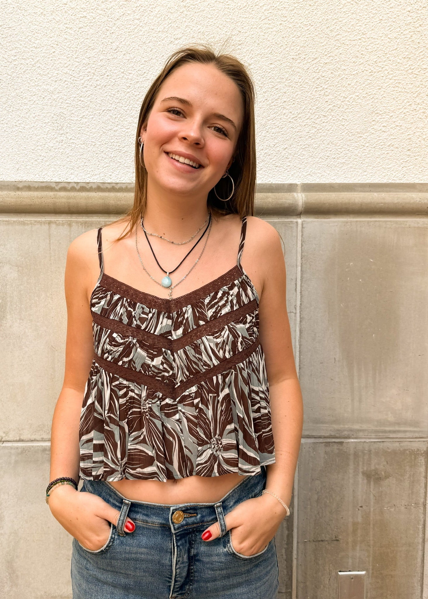Woman wearing a patterned top and jeans standing against a stone wall.