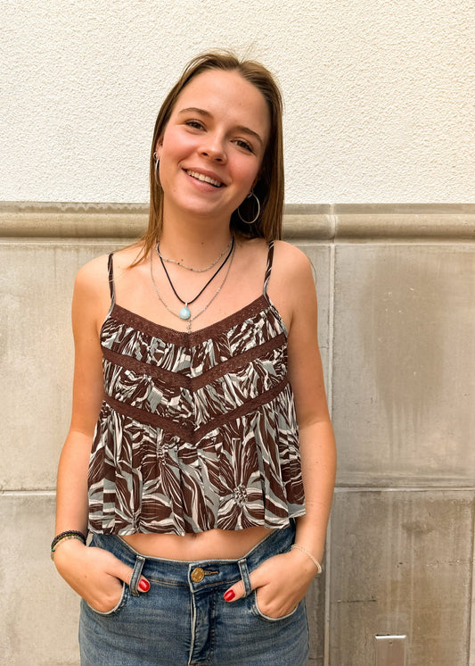 Woman wearing a patterned top and jeans standing against a stone wall.